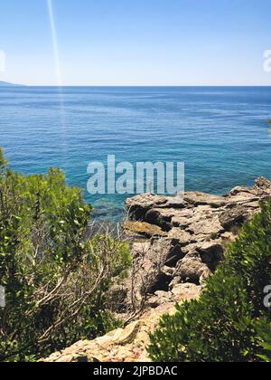 Vecchio hobby pesca pesca pesca in piedi su pietra grande roccia. Anziano pensionato cattura pesce filatura. Vista dall'alto Montenegro Sutomore pietre spiaggia turchese Foto Stock