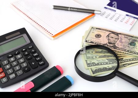 Banconote sparse su un tavolo con una calcolatrice e una lente d'ingrandimento. Foto Stock