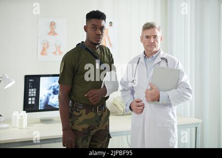 Medico serio e militare ferito con bendaggio su braccio rotto Foto Stock