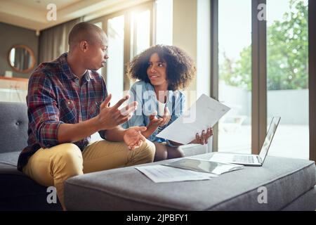 Tutto sta andando secondo il programma. Una giovane coppia allegra che lavora su un laptop e che fa la documentazione insieme mentre è seduto su un divano a casa. Foto Stock