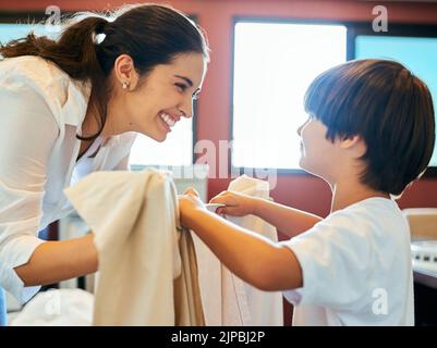 Fare le faccende con il mio ragazzo. Una giovane madre attraente che fa il bucato con il figlio a casa. Foto Stock