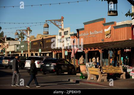 Scottsdale, Arizona, USA - 4 gennaio 2022: La luce del tardo pomeriggio splende sulle facciate storiche della città vecchia, mentre i visitatori attraversano una strada. Foto Stock