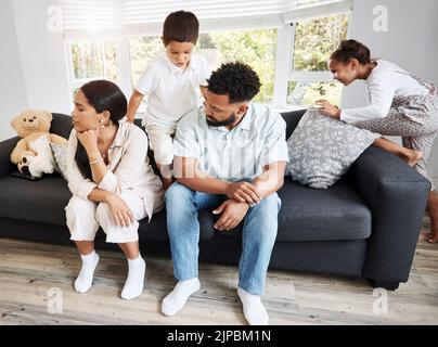 Coppia frustrato, irritata e irritata seduta sul divano con i loro bambini iperattivi, rumorosi e naughty che si ingoolano intorno sul divano a casa. Uomo Foto Stock