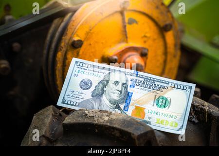 Un centinaio di dollari per primo piano si trovano sulla ruota di un trattore a piedi. Il denaro si trova su uno pneumatico con un grande battistrada nel fango. Finanziamento dell'agricoltura Foto Stock