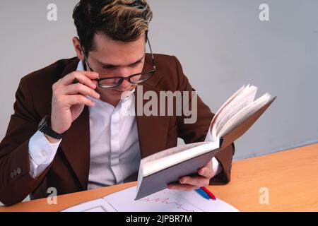 Uomo elegante concentrato che legge alla sua scrivania su uno sfondo bianco. Uomo biondo caucasico che legge nel suo ufficio. Uomo d'affari che lavora nel suo ufficio. Foto di alta qualità Foto Stock