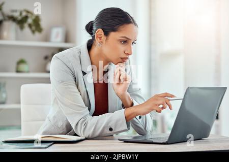 Serio, portatile e donna d'affari professionale seduto e leggere un'e-mail di lavoro con una penna che lavora da casa. Business, computer e donne focalizzate Foto Stock