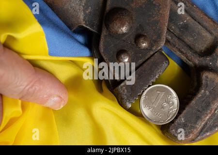 Il gas key tiene il rublo russo sullo sfondo della bandiera dell'Ucraina nelle mani della nonna, il crollo del rublo, sanzioni aga Foto Stock