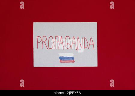 Segnali di carta con slogan propaganda e la bandiera russa su sfondo rosso, azione di protesta, bullshit russo, guerra in Ucraina 2022 Foto Stock