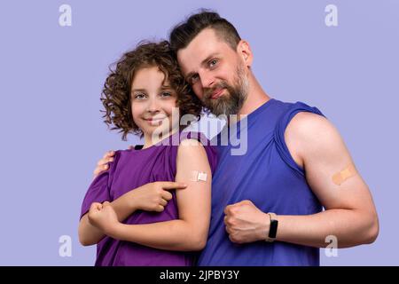 La famiglia della salute in t-shirt di base mostra bicipiti con banda-aiuto dopo l'iniezione del vaccino in lilla studio. Papà e figlia 10-12s vaccinati contro Covid-19 Foto Stock