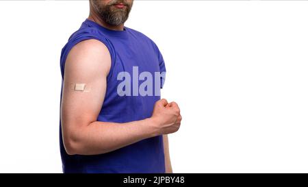 Uomo barbuto irriconoscibile in t-shirt viola con banda-aiuto a portata di mano mantiene il braccio clenches pugno mostra la salute e il potere bicipite dopo la vaccinazione. Preventivo Foto Stock