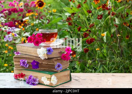 Una tazza di tè su una pila di libri con fiori, giorno estivo soleggiato. Spazio di copia. Foto Stock