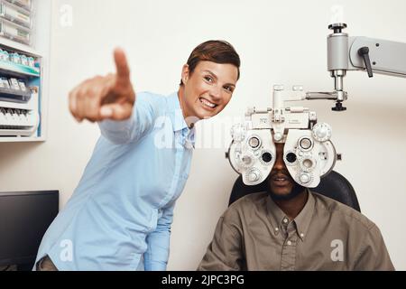 Buon optometristo che fa la prova dell'occhio su un paziente, che esamina la vista e che fa l'esercitazione ottica ad un controllo di optometry. Giovane uomo nero consulenza con un Foto Stock