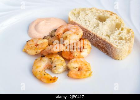 Gamberetti o gamberi arrosto con salsa cocktail e pane su un piatto bianco come antipasto in uno spazio per la copia della cena, focus selezionato, profondità molto stretta di fuoco Foto Stock