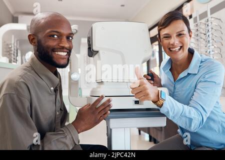 Occhio medico che dà pollici in su dopo un test di visione riuscito con un paziente maschio felice, ritratto. L'optometrista femminile sorridente dà un gesto positivo Foto Stock