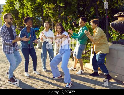 Felici giovani amici multirazziali si incontrano, ballano e divertirsi al parco cittadino in estate Foto Stock