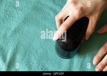 Macchina per la rimozione di pellet su una giacca verde nelle mani di una ragazza, cura dell'abbigliamento Foto Stock