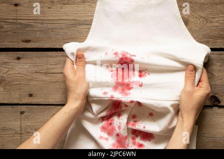 La ragazza tiene in mano un vestito bianco con macchie rosse, lavando vestiti sporchi Foto Stock