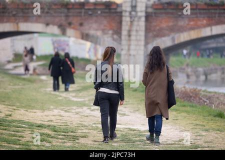 Persone che camminano sul prato lungo le rive di un fiume prosciugato e un ponte sullo sfondo. Foto Stock