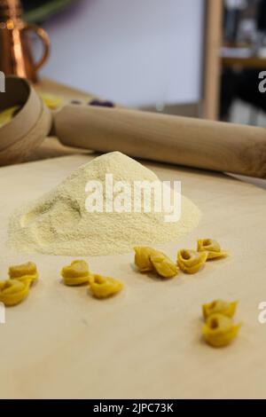 Tortellini crudi appena fatti su tavola di legno e un matterello e farina sullo sfondo. Foto Stock