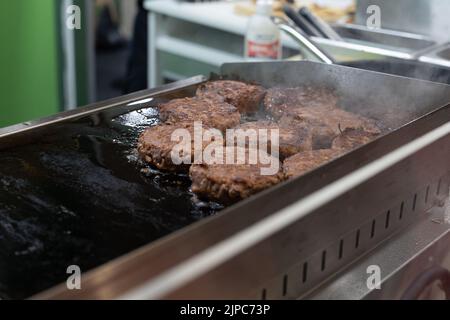 Hamburger ben tostato e capovolto su entrambi i lati che stanno completando la loro cottura su un Griddle caldo. Foto Stock