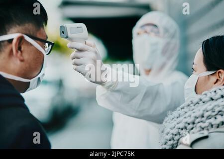 Gli operatori sanitari che testano la temperatura di covid per il protocollo, la conformità o le limitazioni dei paesi in un aeroporto o in una frontiera. Persone che viaggiano all'estero con Foto Stock