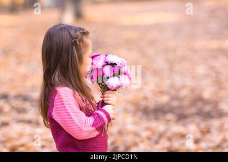 Carina bambina nel parco autunnale con bouquet di fiori rosa. Foto Stock