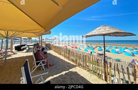 Zandvoort, Paesi Bassi - Agosto 12. 2022: Sedie a sdraio rilassanti sotto gli ombrelloni in bar fronte mare olandese, spiaggia di sabbia, orizzonte del mare nord Foto Stock