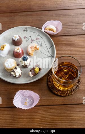 Piccolo bicchiere di cioccolato con crema al pistacchio, accanto a macaron, tartufi, cameo di noce e whiskey glass vertical. Foto Stock