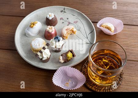 Piccolo bicchiere di cioccolato con crema al pistacchio, accanto a macaron, tartufi, cameo di noce e whiskey glass side view. Foto Stock