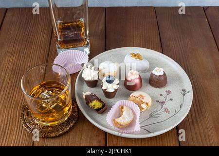 Piccola tazza di cioccolato con crema al pistacchio, accanto a macaron, tartufi, cameo di noce e bicchiere di whiskey e bottiglia. Foto Stock