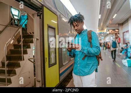 Ragazzo che guarda lo smartphone vicino all'ingresso del treno Foto Stock