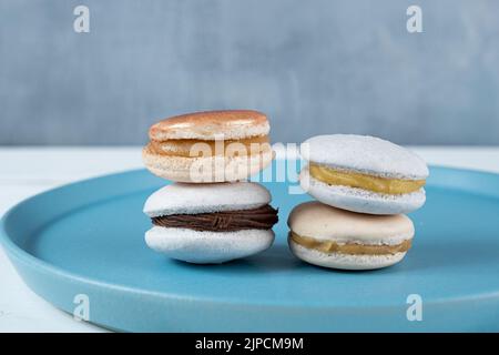 Primo piano di macaron con ripieno di ganache al cioccolato e dulce de leche impilati su un piatto blu. Foto Stock