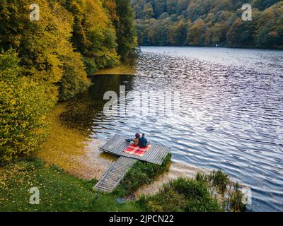 coppia posata sul molo al lago coperto di foglie autunnali Foto Stock