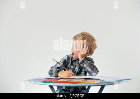 Ragazzo con una matita che sbadigliava a un tavolo, scuola di istruzione Foto Stock