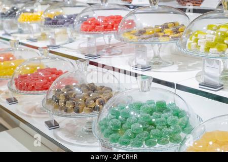 gelatine gommose fatte a mano di diversi colori e sapori in vetrine, bicchiere di vetro pieno di caramelle artigianali, gelatiere gommose con cupole di vetro Foto Stock