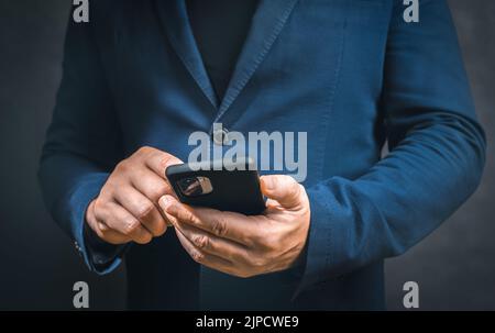 Scatto corto di uomo d'affari usando il cellulare in piedi nel buio. Mano dell'uomo che tiene lo smartphone. Uomo d'affari con telefono cellulare Foto Stock