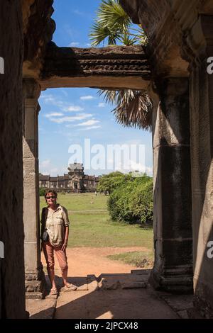 Il turista occidentale si trova all'ingresso rovinato della biblioteca nel cortile esterno di Angkor Wat, Siem Reap, Cambogia Foto Stock