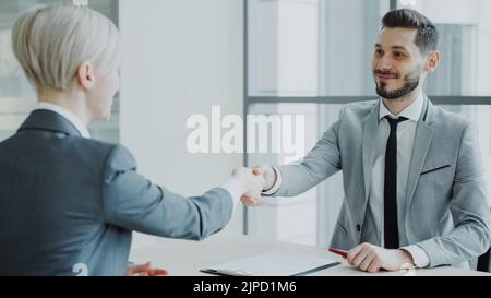 HR manager maschile scuotendo la mano al candidato femminile dopo aver avuto un colloquio di lavoro in un ufficio moderno al coperto Foto Stock