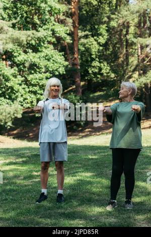 tutta la lunghezza della coppia anziana gioiosa in sport esercitandosi con le mani allungate insieme nel parco Foto Stock