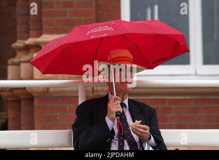 Uno spettatore mangia un panino sotto un ombrello mentre la pioggia smette di giocare durante il giorno uno della prima partita LV= Insurance Test a Lord's, Londra. Data immagine: Mercoledì 17 agosto 2022. Foto Stock