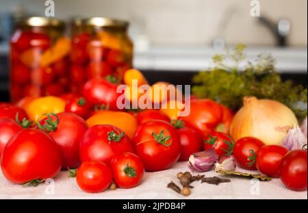 pomodori rossi freschi, spezie, condimenti e pomodori sottaceto in vasetti sul tavolo Foto Stock