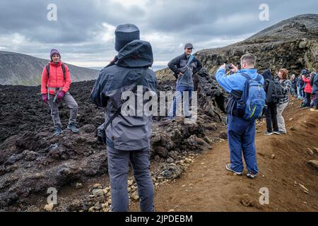 Gli escursionisti sul sentiero per vedere l'eruzione del Vulcano Meradalir in Islanda nell'agosto 2022 si fermano per scattare fotografie sul vecchio campo di lava Foto Stock