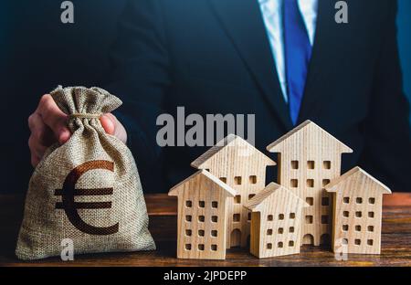 Un uomo d'affari mette un euro borsetta denaro vicino alle case. Investimenti in beni immobili. Bilancio comunale della città. Ufficiale. Industria edile, Foto Stock