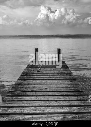 Estate 2022, sull'isola di Wight nel Regno Unito. Una tempesta che passa all'orizzonte e la vista attraverso la calma acqua Solent da un vecchio molo di legno Foto Stock