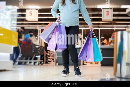 Donna irriconoscibile con pancia che tiene sacchetti di carta dolore durante il fine settimana di shopping per l'acquisto di abbigliamento bambino, immagine ritagliata di mamma che si prepara al bambino hanno parto prematuro nel centro commerciale del negozio Foto Stock