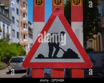 Uomo al lavoro Sign on Road. Cartello segnaletico costruzione su strada stradale sfocata con sfondo colorato bokeh leggero astratto. Copia spazio di trasporto e concetto di viaggio. Foto Stock