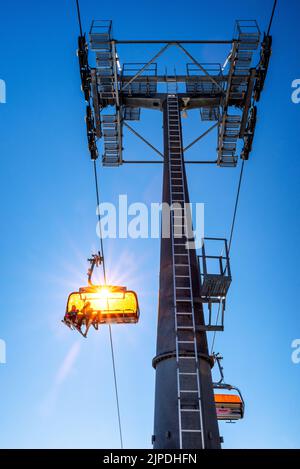 Sciatori seduti alla seggiovia e all'albero della funivia su sfondo blu Foto Stock