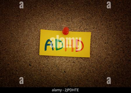 Una nota di carta gialla con l'abbreviazione ADHD su di essa fissata a una tavola di sughero. Primo piano. L'ADHD è un disturbo da deficit di attenzione e iperattività. Foto Stock