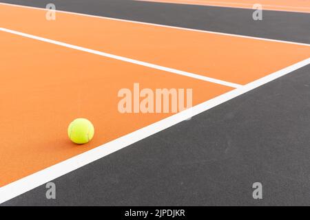 Palla da tennis gialla nel nuovo campo da tennis arancione all'aperto con baseline bianca e nero fuori limite. Foto Stock