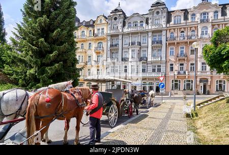 Marienbad, Repubblica Ceca, 30 giugno 2022: Facciate neo-barocche sul bordo della strada dove carrozze trainate da cavalli aspettano i turisti Foto Stock